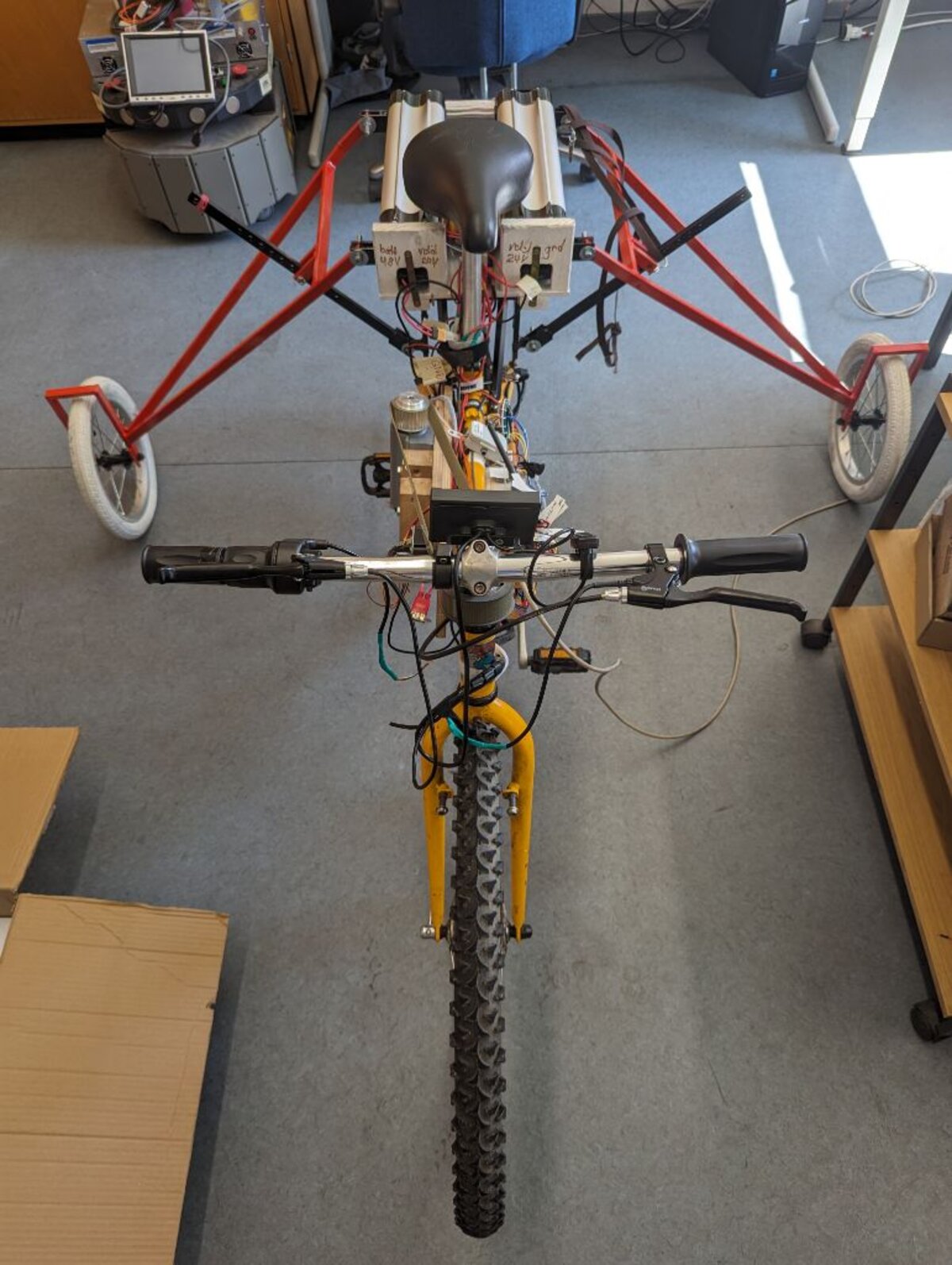 Front-on view of the bicycle with the fork pointed straight ahead, showing the steering motor mounted above the head tube and outrigger training wheels extended to both sides.